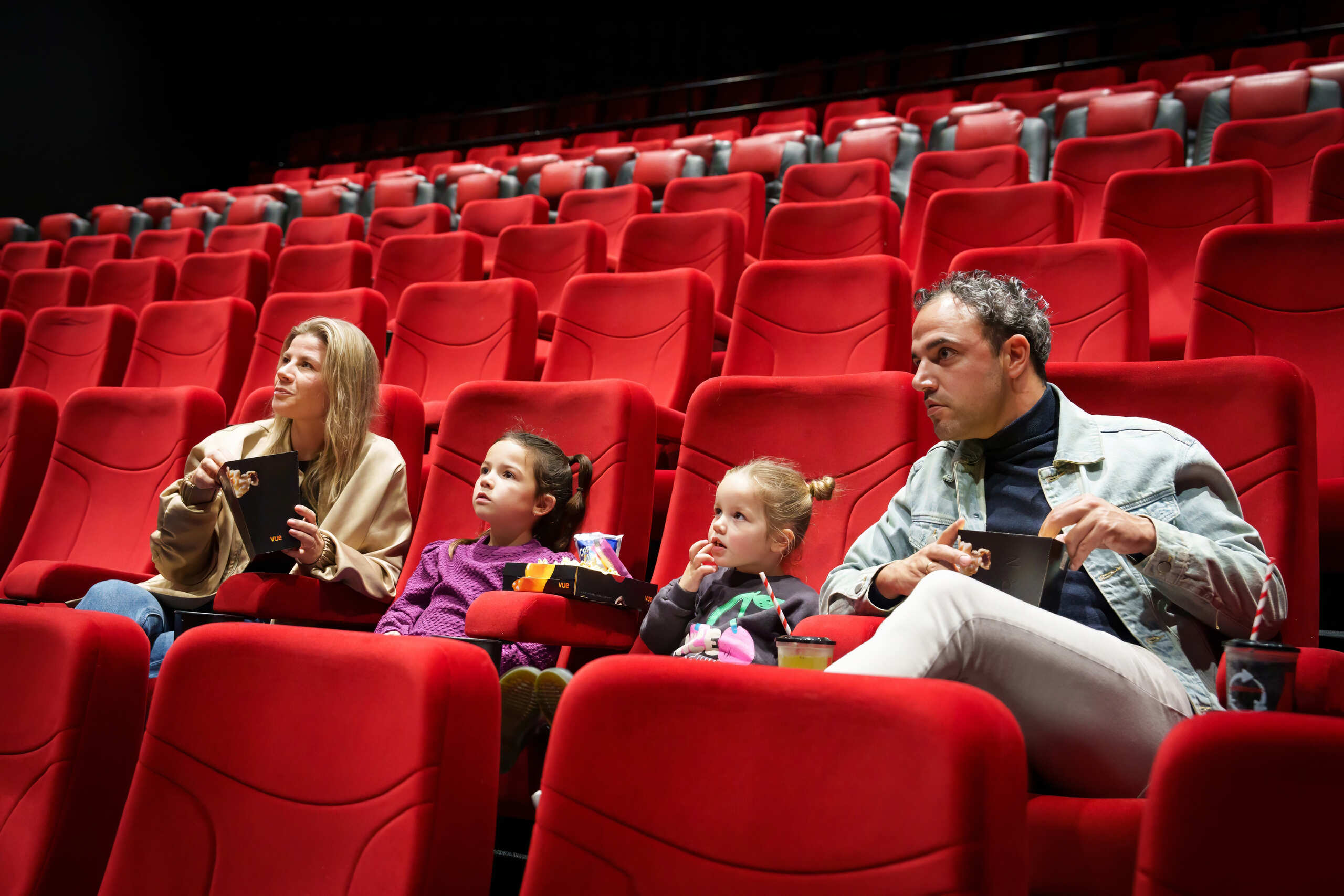 Moeder en vader met kinderen in de bioscoop met popcorn en drinken